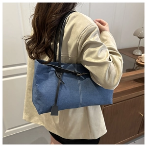 Detail of blue denim tote bag with black leather straps and stylish white contrast stitching