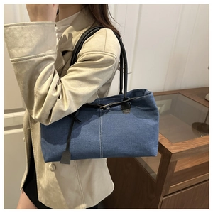 Dettaglio borsa tote in denim blu con manici in pelle nera e cuciture bianche a contrasto
