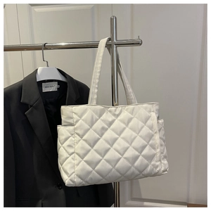 Detailed view of white quilted tote bag with side pocket hanging on a metal rack