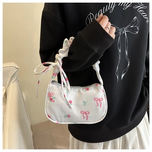 Close-up of a white floral baguette bag with pink roses, bows, and a ruffled strap