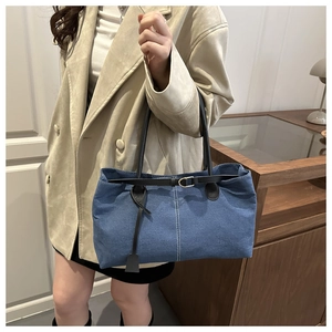 Blue denim tote bag with leather straps and white stitching shown on a shoulder
