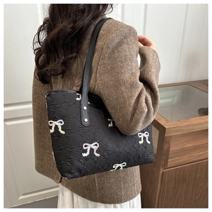 Detail of black tote bag with embossed textures and colorful embroidered bow motifs