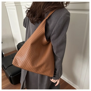 Detail view of woven leather texture on a tan oversized shoulder tote bag worn by model