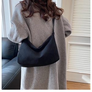 Model wearing black suede crescent tote bag showing back view and shoulder strap details