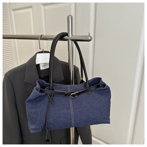 Detail of blue denim tote bag with leather strap and gold metal buckle on display