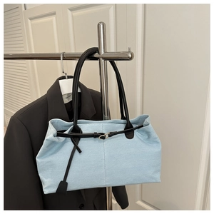 Close-up of light blue denim tote bag with black leather handles hanging in a closet