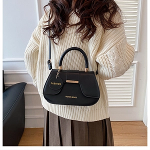 Detail of a black PU leather saddle bag with a round handle and metal fashion charm