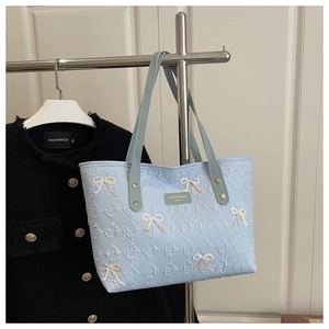 Detailed view of light blue embossed leather tote with sequined bow and metal plaque