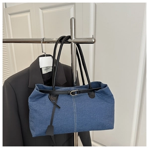 Detailed view of blue denim tote bag with black leather straps and gold buckles