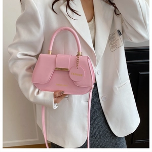 Close-up of pale pink saddle bag with gold hardware and fashion charms on white blazer