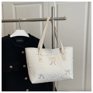 Close-up of white tote bag with colorful bow embroidery and textured leather surface