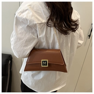 Detail of caramel brown crossbody bag with gold M-buckle on white shirt background