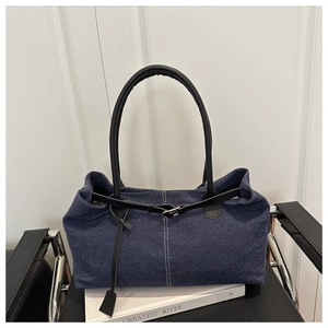 Detail of dark blue denim tote bag with black leather straps on a leather chair