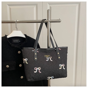 Detail of black quilted tote bag with colorful butterfly embroidery and metal nameplate
