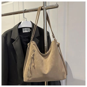 Détail du sac Hobo kaki avec fermeture éclair verticale et pompon sur fond de costume