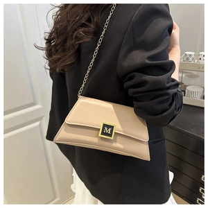 Detail of apricot chain bag with gold M-logo buckle worn over a black suit blazer