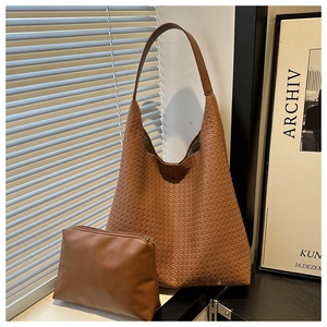 Gros plan sur le sac fourre-tout tressé marron et sa pochette assortie sur une table noire