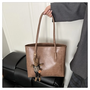 Close-up of brown faux leather tote bag with a cute rabbit plush charm and stitching details