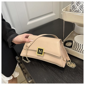 Close-up of beige pillow bag featuring gold M-logo metal clasp and chain strap