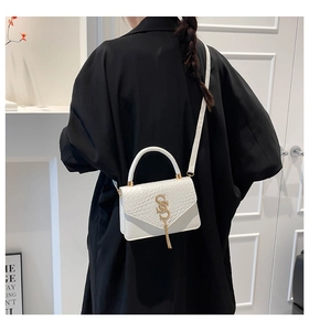 Gros plan d'un sac bandoulière blanc gaufré avec logo doré et pompon sur le mannequin