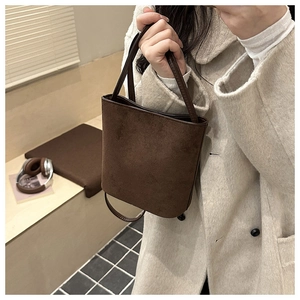 Close-up of a brown suede bucket bag worn with a beige coat in a cozy indoor setting