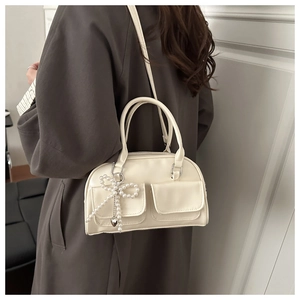 Detail of cream Boston bag with pearl bow pendant and decorative front pockets