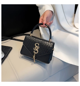 Detail of black crossbody bag with crocodile texture flap, gold hardware, and tassel