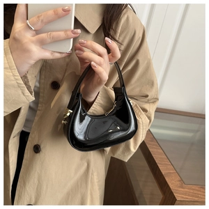 Detail of glossy black patent leather hobo bag with gold zipper held by a model