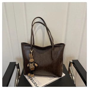 Detail of a dark brown vintage tote bag with a cute bunny charm on a modern black chair