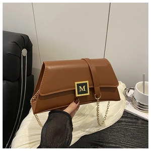 Detailed macro view of the golden M logo buckle and smooth caramel leather on the handbag