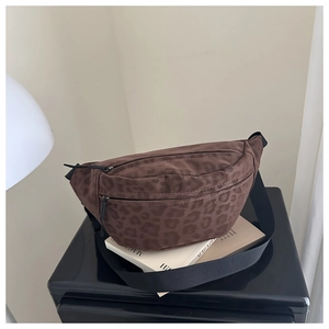 Detail of leopard print waist bag with dual zippers and adjustable nylon strap on a book