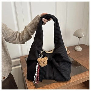 Detail of black corduroy tote bag featuring a large bow and a cute plush bear charm