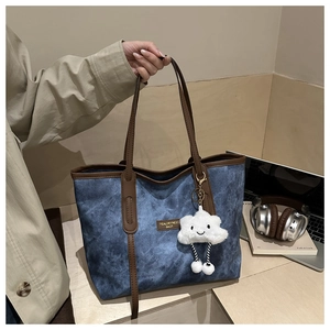 Close-up of blue denim tote bag with brown leather handles and a plush cloud charm