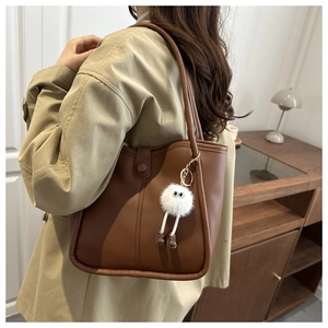 Close-up of brown leather bucket bag featuring a white plush monster charm and stitching