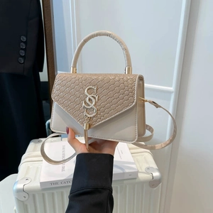 Beige patchwork crossbody bag with woven flap and gold 'S' hardware on suitcase