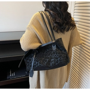 Close-up of leopard print tote bag with leather strap worn over a beige sweater