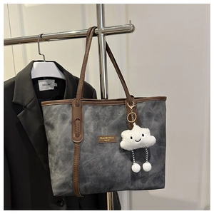 Detail of grey tote bag with leather straps and plush charm hanging on a rack