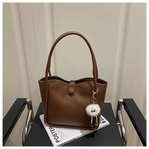 Retro brown leather tote bag detail with white plush monster charm on a chair