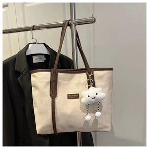 Detail of off-white canvas tote bag with brown leather handles and cloud plush charm