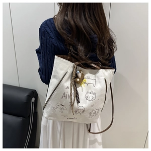Detail of canvas tote bag featuring cartoon patterns and a brown plush bear charm