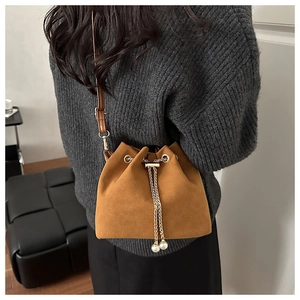 Detail of brown suede bucket bag featuring golden chain drawstring and pearl pendant