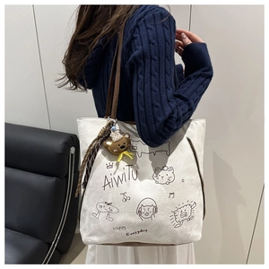 Detailed view of cream canvas tote bag with brown straps and cute bear pendant