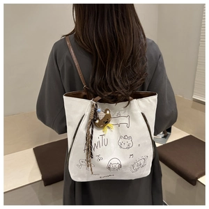 Close-up of white canvas tote with cartoon illustrations and bear plush keychain