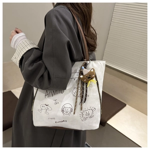 Detail of white tote bag with cute doodle prints and a plush bear pendant on side