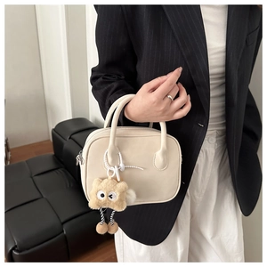 Detail van beige Boston tas met harige monsterhanger en gladde matte textuurafwerking