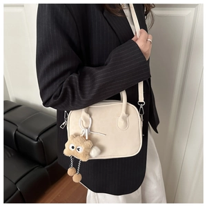 Detail of off-white matte shoulder bag with a cute brown plush bear charm accessory