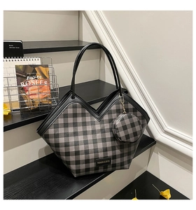 Detail view of large plaid tote bag with V-shaped opening and round charm on stairs