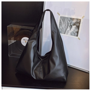 Detail of a large black leather hobo bag on a wooden table in a minimalist setting