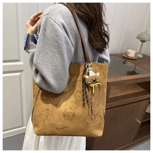 Detail of a brown suede tote bag with cartoon graphics and a cute 3D bear plush charm