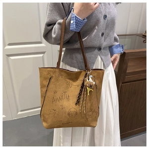 Detail of brown tote bag featuring hand-drawn graffiti graphics and a cute plush bear charm